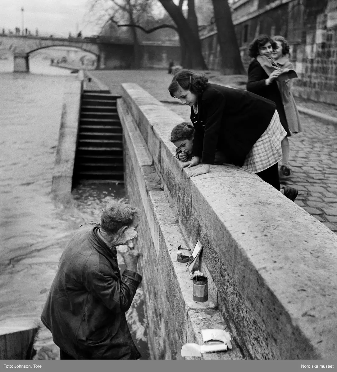 Paris. En man rakar sig vid kajen längs Seine iakttagen av några flickor.