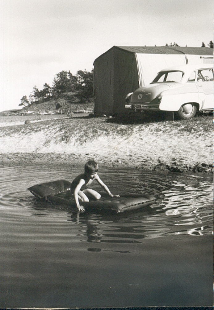 Telttur, gutt på gummimadrass, bading i sjøen, bil parkert ved vannkanten.