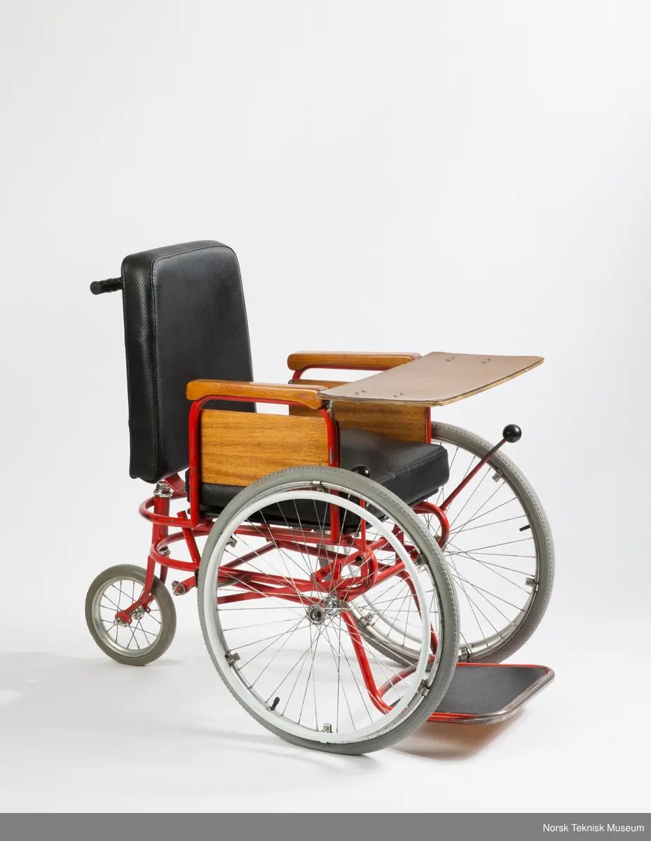 Rullestolen er i metall og mørkt tre, og stilen er funkis.
Terje har malt metallet rødt (opprinnelig farge kan ses bak, ved skruefestet) og pusset og lakket armlenene, ellers er den original.