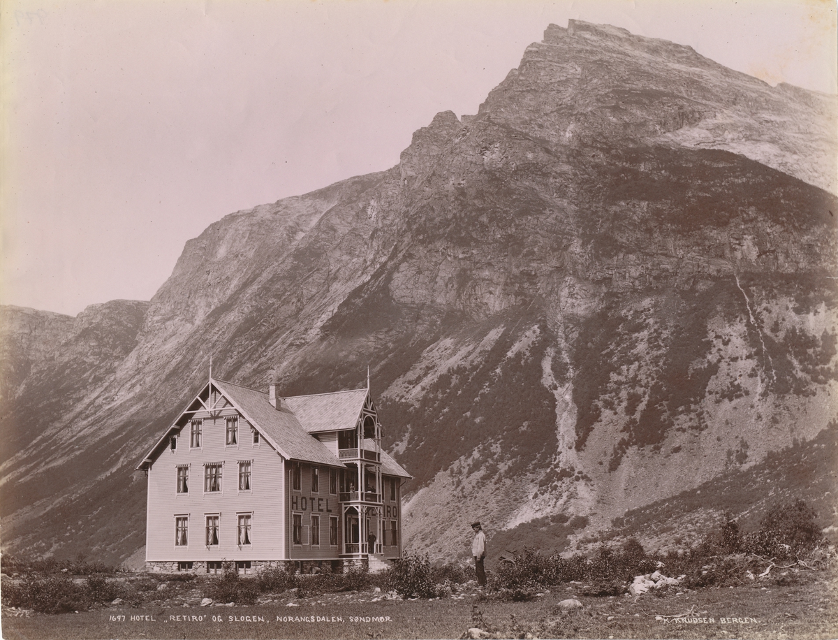 Prospektfotografi av Hotell Retiro med fjellet Slogen i Norangsdalen. En mann står utenfor hotellet.