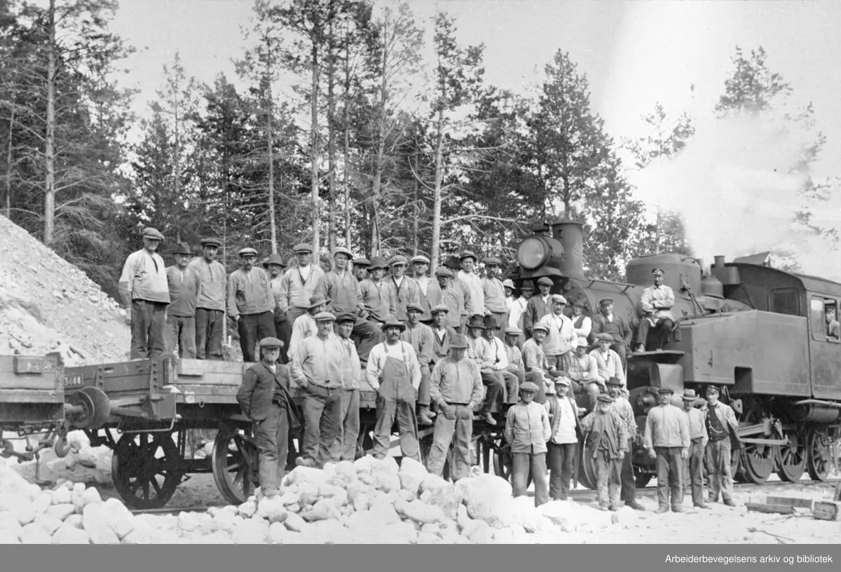 Fra anlegget av Raumabanen ved Jora grustak, 1921. Til høyre foran: Lokomotivfører Sigvald Gulbrandsen. I lokomotiv vinduet fyrbøter Oskar Larsen, på vogntaket konduktør Oskar Olsen.