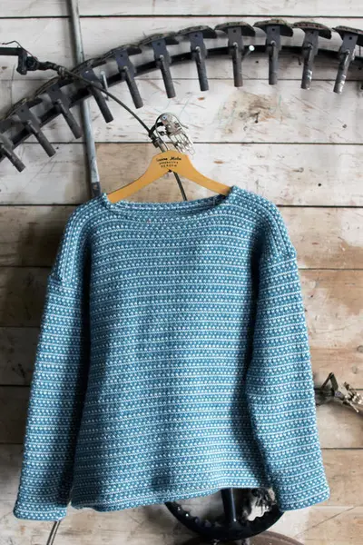 blå ullgenser heng på vegg mellom maskindelar