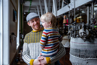 mann og barn i fabrikklokale med strikkemaskiner