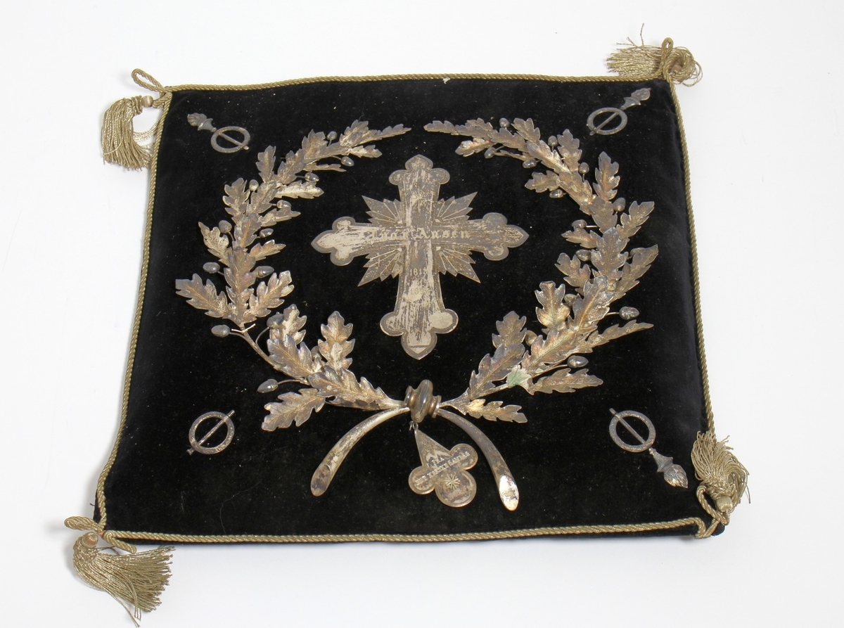 Bårekrans frå Ivar Aasen si gravferd i 1896. Aasen døydde 23. september 1896, og det var gravferd frå Vår Frelsars gravlund 29. september. (1) På kransen kan vi sjå ein kross i sølv med det følgjande gravert inn: "Ivar Aasen 1813-1896." Under krossen finn vi teksten: "Fra Det Norske Samlag."

Kjelde:
https://www.sprakradet.no/Vi-og-vart/Publikasjoner/Spraaknytt/Arkivet/Spraaknytt_1996/Spraaknytt_1996_1/Om_Ivar_Aasen_i_eit_minneaar/ (Lesedato: 15.10.2020)