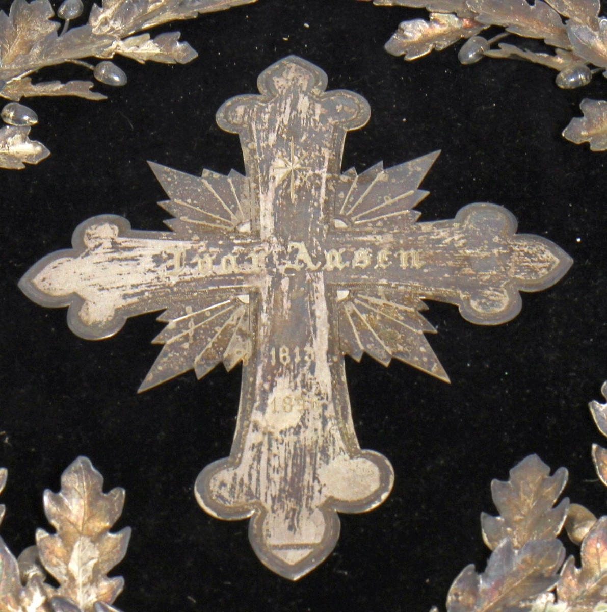 Bårekrans frå Ivar Aasen si gravferd i 1896. Aasen døydde 23. september 1896, og det var gravferd frå Vår Frelsars gravlund 29. september. (1) På kransen kan vi sjå ein kross i sølv med det følgjande gravert inn: "Ivar Aasen 1813-1896." Under krossen finn vi teksten: "Fra Det Norske Samlag."

Kjelde:
https://www.sprakradet.no/Vi-og-vart/Publikasjoner/Spraaknytt/Arkivet/Spraaknytt_1996/Spraaknytt_1996_1/Om_Ivar_Aasen_i_eit_minneaar/ (Lesedato: 15.10.2020)