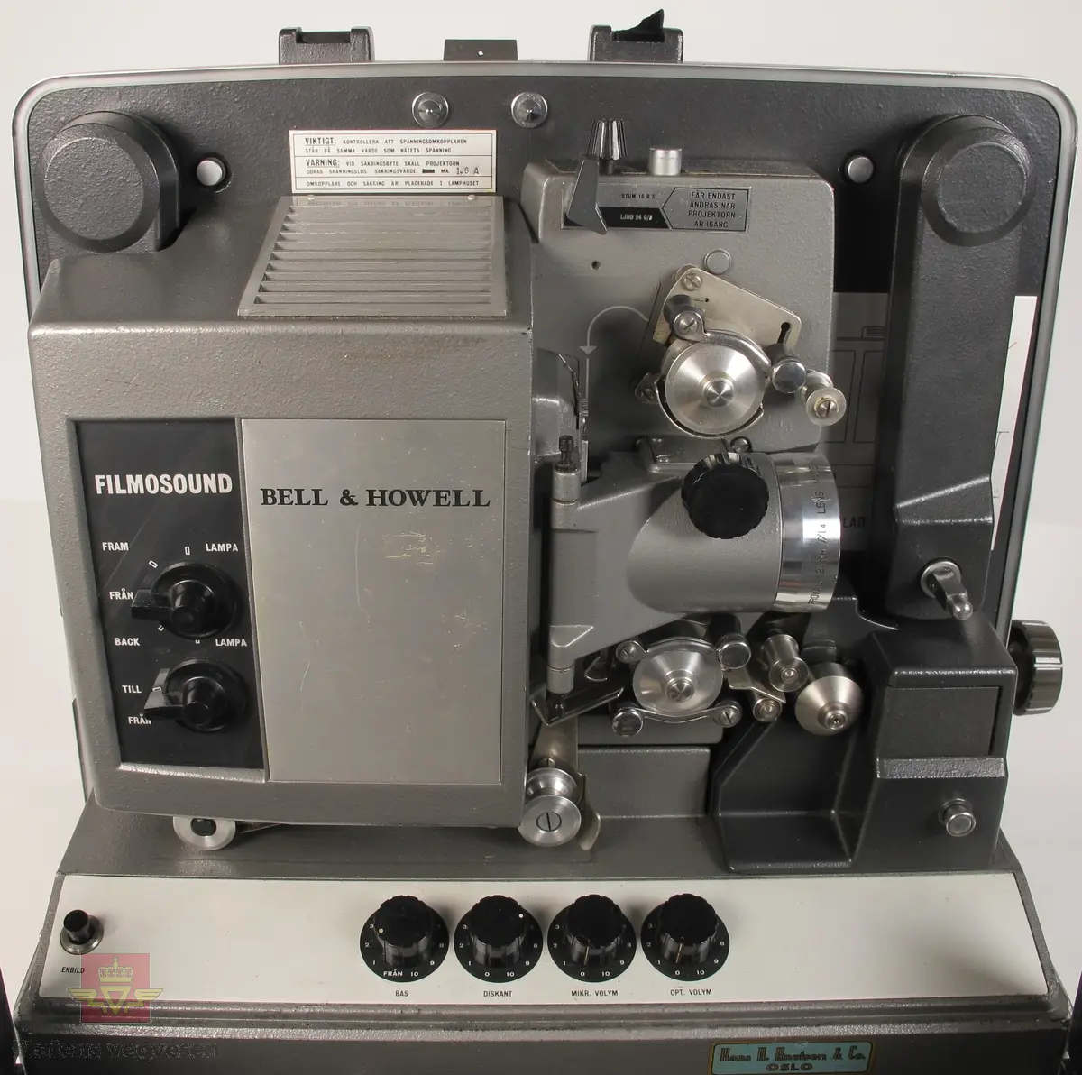 BELL & HOWELL MODEL 642. 16 mm filmfremviser i mørk grå koffert av glassfiber, med defekt bærehåndtak. Den ene delen av kofferten har høyttaler av merket Goodmans, ledning for tilkobling av høyttaler og to klistremerker med påskrifter. Filmfreviseren har eget panel for justering av lyden. Bak på kofferten er det to skiltplater med innskrifter, MODEL 642 SK SERIAL No. K418 220V-1100 W - 50 ~ MADE IN ENGLAND og HANS H. KNUTSEN & CO. OSLO TYPE 642 No 418 P.VOLT 200/250 50 ~ S.VOLT AMP. 1200W. Veske, strømledning, ekstra lyspære og to tomme filmruller følger med filmfremviseren.