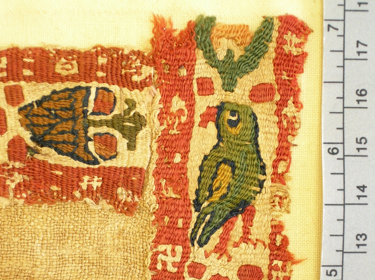Tuskaft med påsydda bårder och bladformad medaljong i gobelängteknik.
Varp (bottenväv): ca 13 tr/cm S-spunnet 1-tr lin, naturfärgat.
Inslag (bottenväv): ca 18 tr/cm S-spunnet 1-tr lin, naturfärgat.
Varp (gobelängväv): S-spunnet 1-tr lin, naturfärgat. Varptrådarna går 2 och 2.
Inslag (gobelängväv): S-spunnen 1-tr ull, röd, rosa, gul, orange, brun, grön, gulgrön, mörkturkos och mörkblå.
I mitten bladformat medaljong med 2 par motställda fåglar i grönt och mörkturkos med blomfigur emellan sig. Inramad med 10 mm bred kant i rött med små rektanglar i lintråd.
Runt alla 4 sidor ca 30 mm breda bårder med blommor och fåglar. På varje bård 5 mm breda röda kanter med småmotiv i lintråd; hakkors, fyrkanter, spetsformad figur.