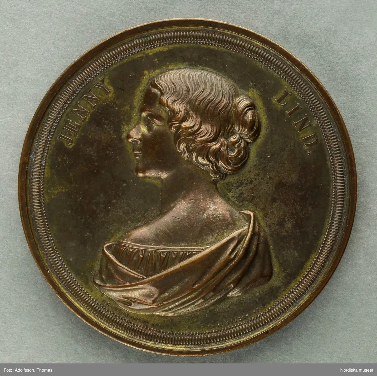 Huvudliggaren:
"Minnespenning. I brons. Öfver Jenny Lind, henne tillegnad af tonkonstens vänner i Stockholm. Jmfr. Hildebrand, B.E. 'Minnespenningar öfver enskilda svenska män och kvinnor' sid. 364, nr 5. G. af fabrikör A. Fagerberg 29/3 1876."

Med etui.
/Ingrid Frankow 2007-05-04