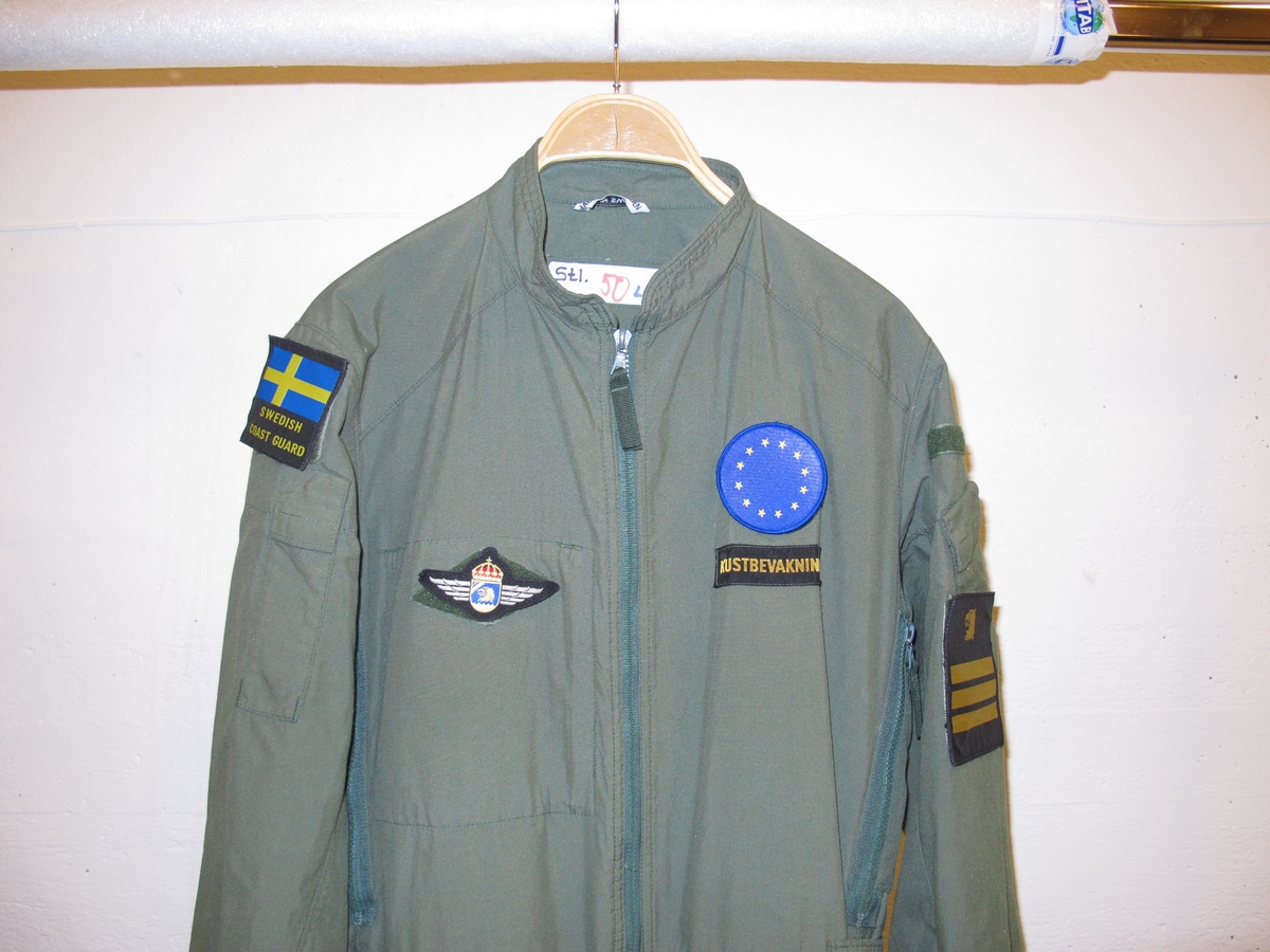 Overall, grön med emblém. På höger ärm svensk flagga med texten "Swedish coast guard" undertill. 
På höger ärm Kustbevakningens örnhuvud och gradbeteckning.
På höger bröst emblém: Kustbevakningen flyg.
På vänter bröst rund EU-flagga och där under textband "Kustbevakningen". Av bomullsmix.