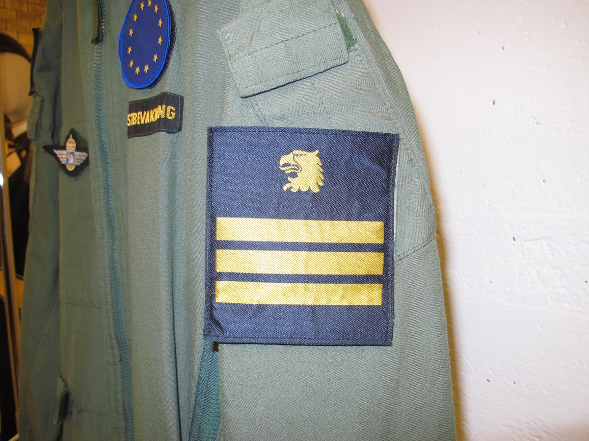 Overall, grön med emblém. På höger ärm svensk flagga med texten "Swedish coast guard" undertill. 
På höger ärm Kustbevakningens örnhuvud och gradbeteckning.
På höger bröst emblém: Kustbevakningen flyg.
På vänter bröst rund EU-flagga och där under textband "Kustbevakningen". Av bomullsmix.
