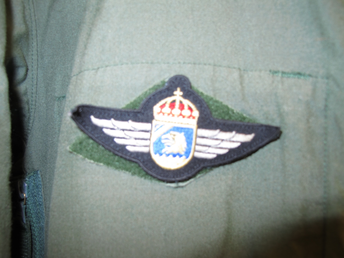 Overall, grön med emblém. På höger ärm svensk flagga med texten "Swedish coast guard" undertill. 
På höger ärm Kustbevakningens örnhuvud och gradbeteckning.
På höger bröst emblém: Kustbevakningen flyg.
På vänter bröst rund EU-flagga och där under textband "Kustbevakningen". Av bomullsmix.