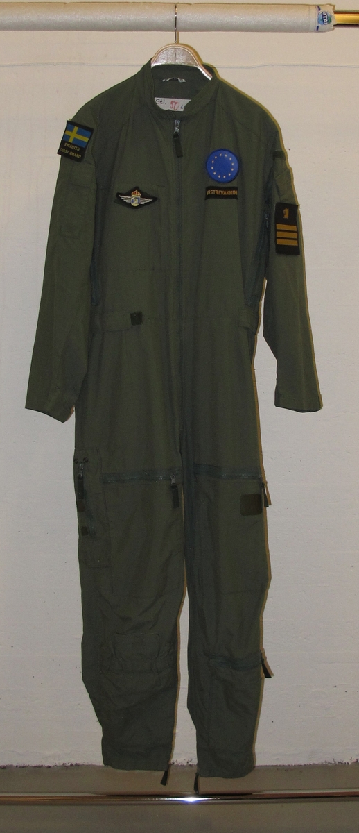 Overall, grön med emblém. På höger ärm svensk flagga med texten "Swedish coast guard" undertill. 
På höger ärm Kustbevakningens örnhuvud och gradbeteckning.
På höger bröst emblém: Kustbevakningen flyg.
På vänter bröst rund EU-flagga och där under textband "Kustbevakningen". Av bomullsmix.