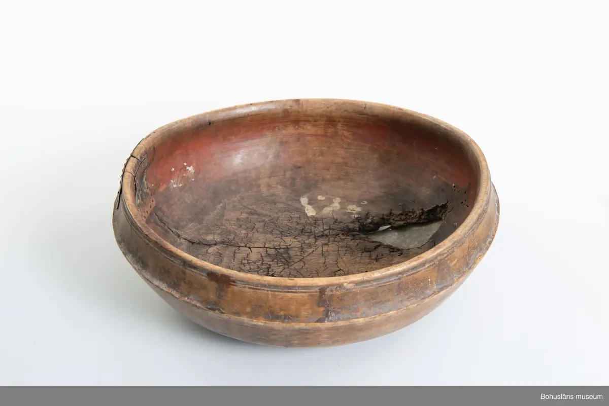Rund svarvad skål med indragen öppning. Linjedekor på utsidan  samt fotring nertill.
Har varit målad med roströd färg.
Tre lagningar med plåt upptill vid kanten samt en under botten,  där en bit trä saknas. Små sprickor i botten på grund av användning.
Synliga skadedjursangrepp.

Litt.; Kjellberg, Sven T, Ölets käril - Om skålen, bollen och  hanapen, Kulturen 1964, Lund 1964, s. 36-48.

Ur handskrivna katalogen 1957-1958:
Träskål, plåtbeslagen
Diam. 28,5.29. Har invändigt åtminstone delvis varit rödfärgad. Ett hål i botten, en större spricka, enstaka maskhål.

Lappkatalog: 67