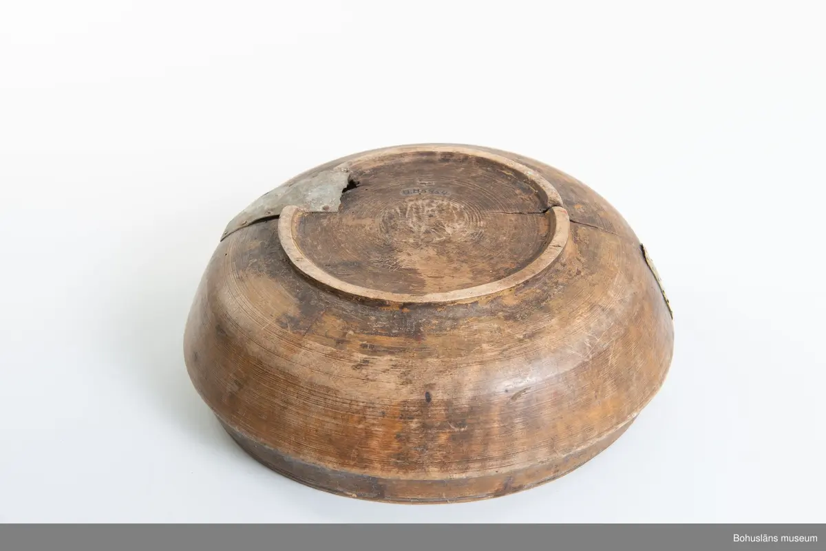 Rund svarvad skål med indragen öppning. Linjedekor på utsidan  samt fotring nertill.
Har varit målad med roströd färg.
Tre lagningar med plåt upptill vid kanten samt en under botten,  där en bit trä saknas. Små sprickor i botten på grund av användning.
Synliga skadedjursangrepp.

Litt.; Kjellberg, Sven T, Ölets käril - Om skålen, bollen och  hanapen, Kulturen 1964, Lund 1964, s. 36-48.

Ur handskrivna katalogen 1957-1958:
Träskål, plåtbeslagen
Diam. 28,5.29. Har invändigt åtminstone delvis varit rödfärgad. Ett hål i botten, en större spricka, enstaka maskhål.

Lappkatalog: 67