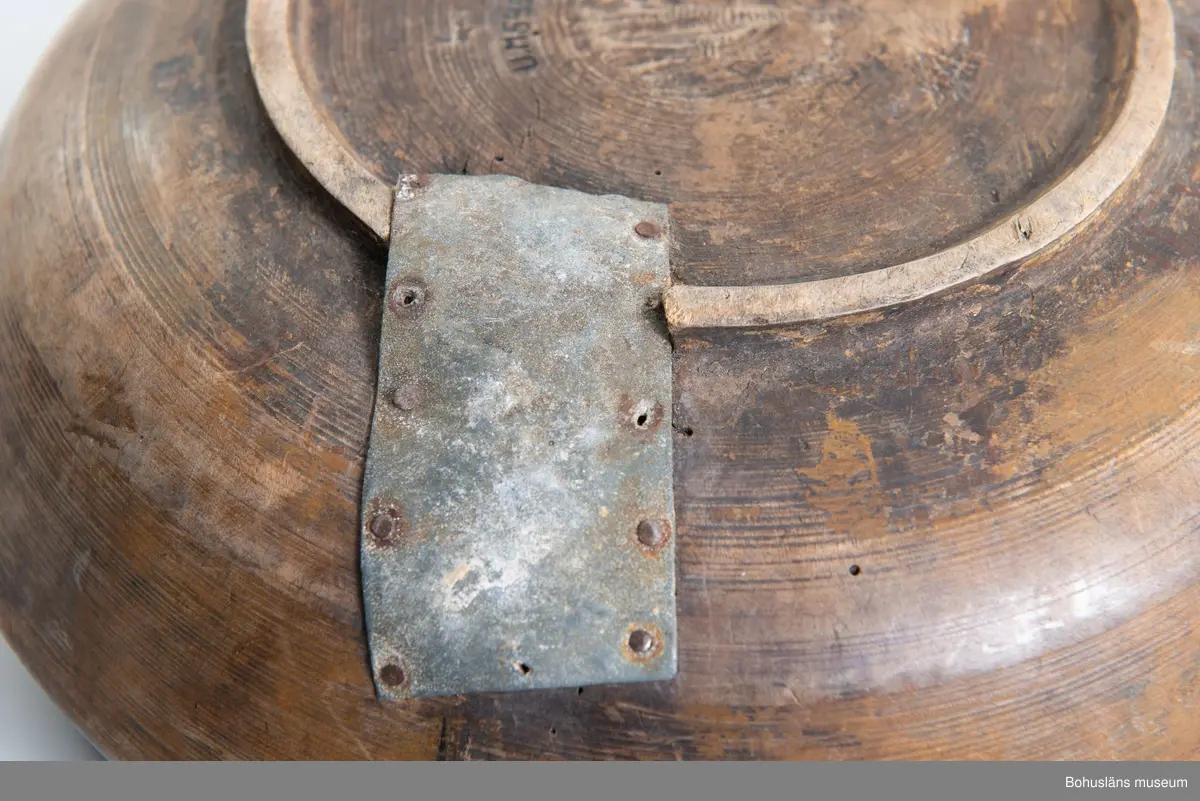 Rund svarvad skål med indragen öppning. Linjedekor på utsidan  samt fotring nertill.
Har varit målad med roströd färg.
Tre lagningar med plåt upptill vid kanten samt en under botten,  där en bit trä saknas. Små sprickor i botten på grund av användning.
Synliga skadedjursangrepp.

Litt.; Kjellberg, Sven T, Ölets käril - Om skålen, bollen och  hanapen, Kulturen 1964, Lund 1964, s. 36-48.

Ur handskrivna katalogen 1957-1958:
Träskål, plåtbeslagen
Diam. 28,5.29. Har invändigt åtminstone delvis varit rödfärgad. Ett hål i botten, en större spricka, enstaka maskhål.

Lappkatalog: 67