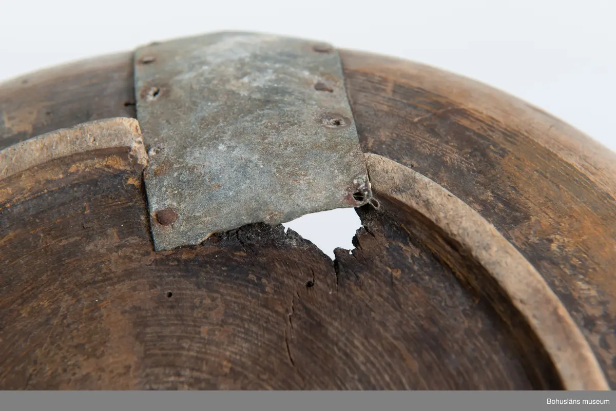 Rund svarvad skål med indragen öppning. Linjedekor på utsidan  samt fotring nertill.
Har varit målad med roströd färg.
Tre lagningar med plåt upptill vid kanten samt en under botten,  där en bit trä saknas. Små sprickor i botten på grund av användning.
Synliga skadedjursangrepp.

Litt.; Kjellberg, Sven T, Ölets käril - Om skålen, bollen och  hanapen, Kulturen 1964, Lund 1964, s. 36-48.

Ur handskrivna katalogen 1957-1958:
Träskål, plåtbeslagen
Diam. 28,5.29. Har invändigt åtminstone delvis varit rödfärgad. Ett hål i botten, en större spricka, enstaka maskhål.

Lappkatalog: 67