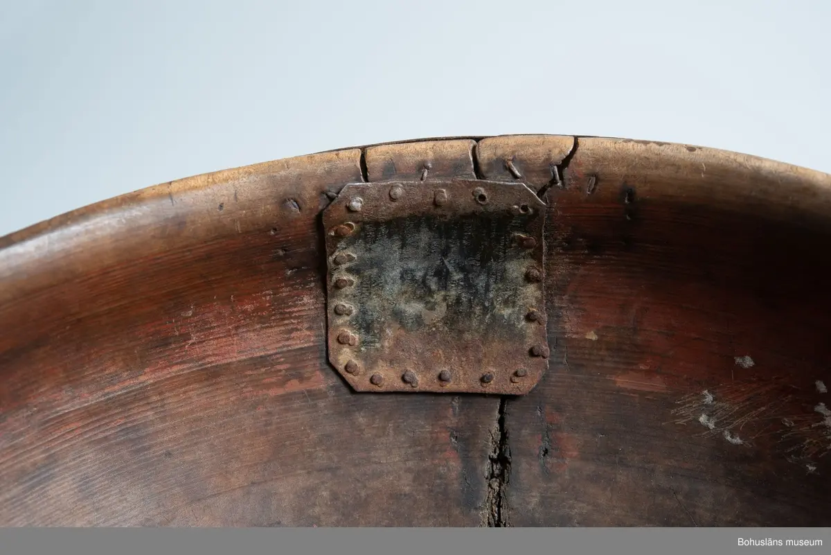 Rund svarvad skål med indragen öppning. Linjedekor på utsidan  samt fotring nertill.
Har varit målad med roströd färg.
Tre lagningar med plåt upptill vid kanten samt en under botten,  där en bit trä saknas. Små sprickor i botten på grund av användning.
Synliga skadedjursangrepp.

Litt.; Kjellberg, Sven T, Ölets käril - Om skålen, bollen och  hanapen, Kulturen 1964, Lund 1964, s. 36-48.

Ur handskrivna katalogen 1957-1958:
Träskål, plåtbeslagen
Diam. 28,5.29. Har invändigt åtminstone delvis varit rödfärgad. Ett hål i botten, en större spricka, enstaka maskhål.

Lappkatalog: 67