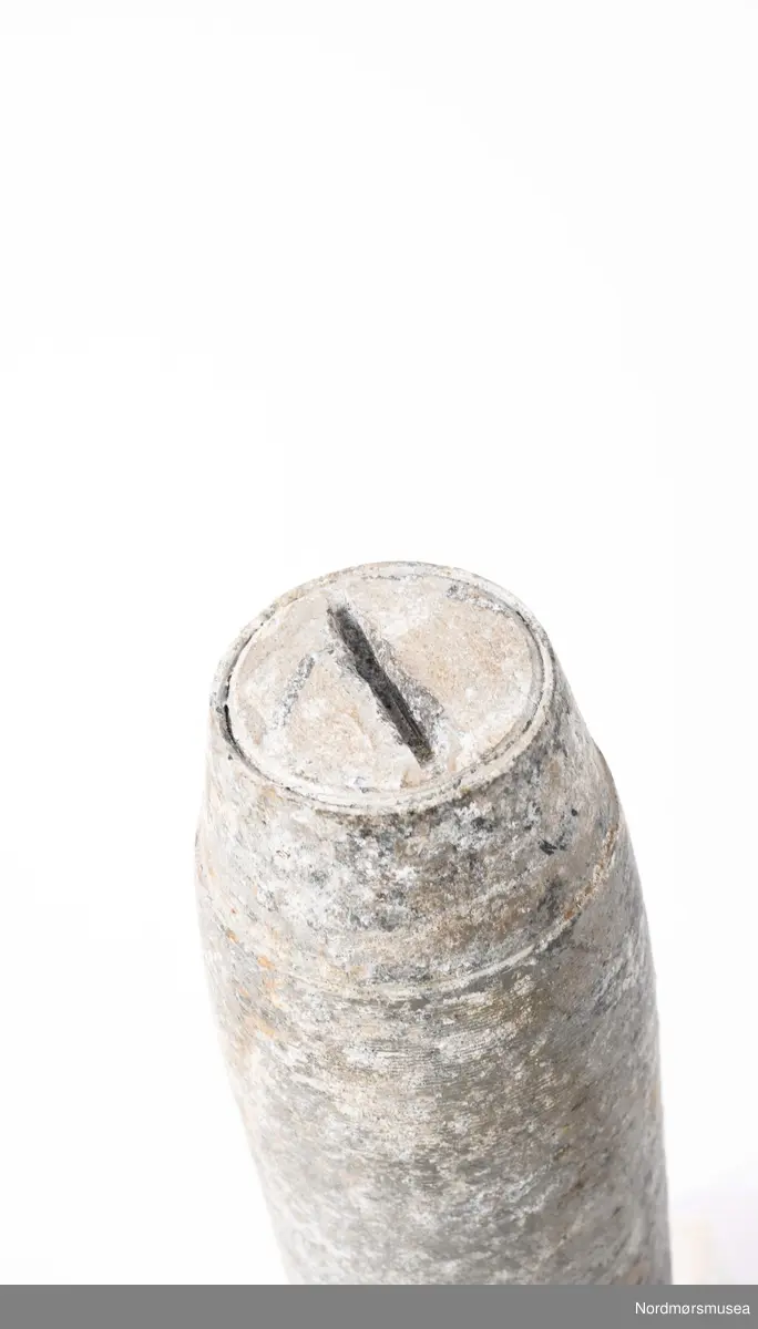 Tysk brannbombe sluppet fra tyske fly (sannsynligvis Heinkel 111 flystasjonert på Værnes) fra aprildagene i Kristiansund 1940. En av de få som ikke virket. Bakerste del mangler. Sylindirsk med flat bunn og topp. Avsmalnende felt bak for feste av framstykke. I motsatt ende er det 6 hull og to mindre lenger ned. Se foto KMb-1987-005.1963