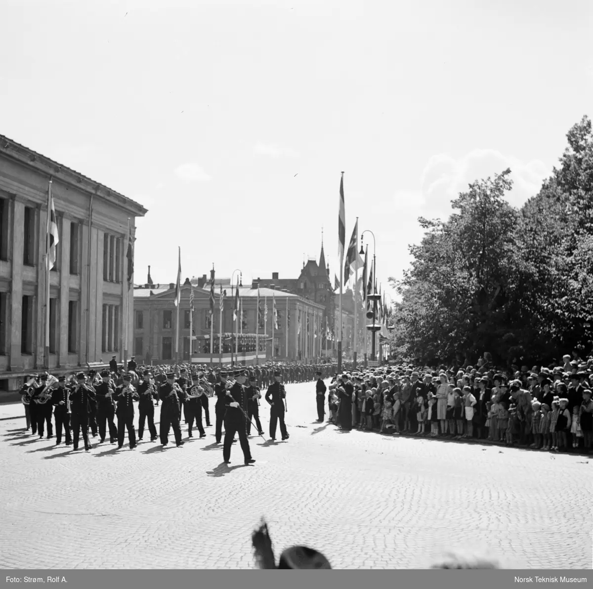 Opptog, USAs nasjonaldag, politi eller militært musikkorps, foran marsjerende soldater, tilskuere, ærestribune, norske, amerikanske og andre nasjonaliteters flagg, ved Universitetet i Oslo, 4. juli 1945.