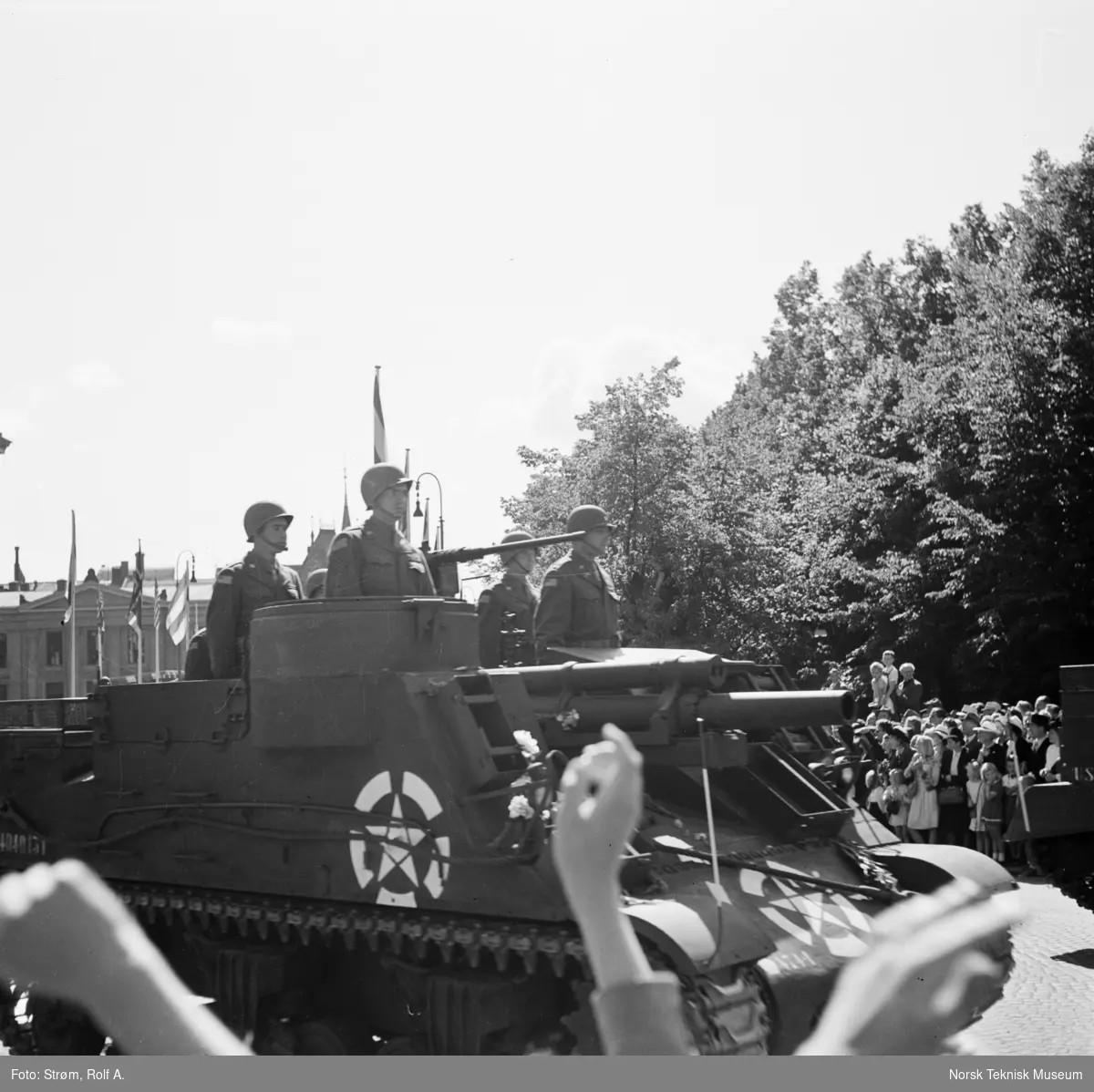 Opptog, USAs nasjonaldag, tanks med stående soldater passerer tilskuere ved Universitetet, gata er pyntet med norske, amerikanske og andre nasjonaliteters flagg,  Oslo, 4. juli 1945.