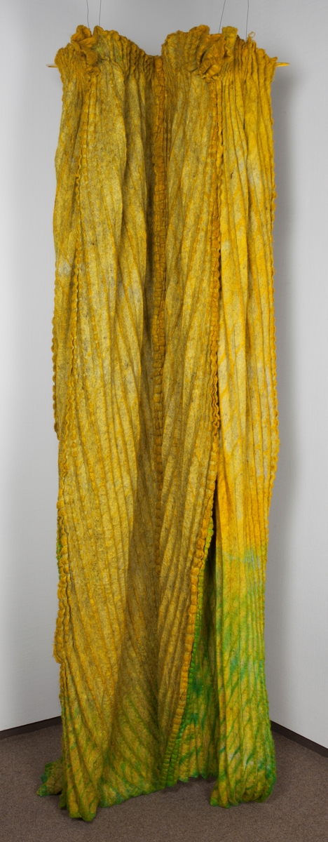 Fritthengende, tekstilt kunsthåndverk av plissert og tovet ull. Objektet er skulpturelt av uttrykk og utstyrt med løpegang øverst, og tredd på en åpen metallring. Fremstår dermed som et sylindrisk, halvveis lukket rom fra tak til gulv. Tekstilet er svært tungt og kraftig tovet, sammensatt av fire lengder. Disse er sydd sammen for hånd, slik at sømmonnene fremstår som bølgete kanter på rettsiden. Tekstilet er sennepsgult, men går nederst over i svakt limegrønt på sidene og baksiden. Det limegrønne er overskåret av parallelle og diagonale striper i skarpere grønt. Disse stripene krysser plisseringen, slik at det dannes et optisk inntrykk av rombeformede ruter.