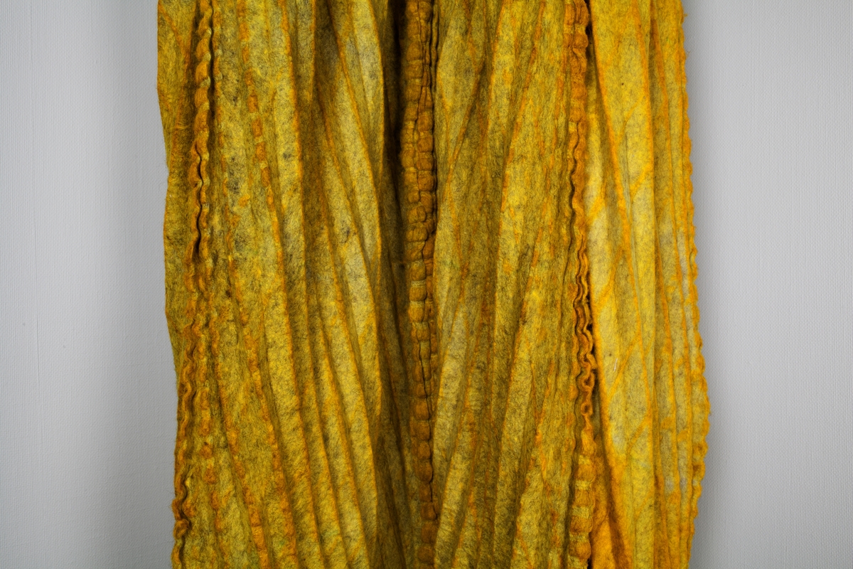 Fritthengende, tekstilt kunsthåndverk av plissert og tovet ull. Objektet er skulpturelt av uttrykk og utstyrt med løpegang øverst, og tredd på en åpen metallring. Fremstår dermed som et sylindrisk, halvveis lukket rom fra tak til gulv. Tekstilet er svært tungt og kraftig tovet, sammensatt av fire lengder. Disse er sydd sammen for hånd, slik at sømmonnene fremstår som bølgete kanter på rettsiden. Tekstilet er sennepsgult, men går nederst over i svakt limegrønt på sidene og baksiden. Det limegrønne er overskåret av parallelle og diagonale striper i skarpere grønt. Disse stripene krysser plisseringen, slik at det dannes et optisk inntrykk av rombeformede ruter.