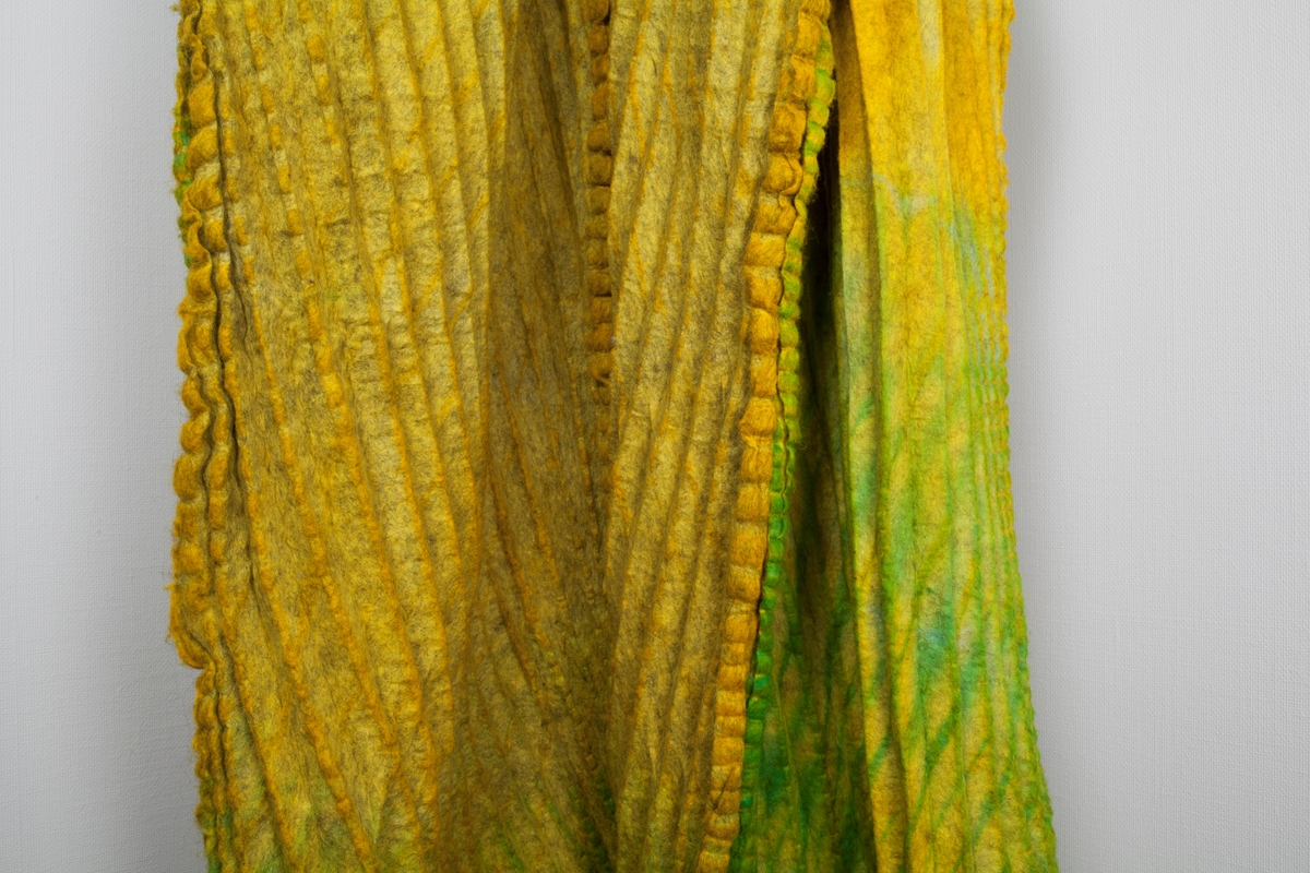 Fritthengende, tekstilt kunsthåndverk av plissert og tovet ull. Objektet er skulpturelt av uttrykk og utstyrt med løpegang øverst, og tredd på en åpen metallring. Fremstår dermed som et sylindrisk, halvveis lukket rom fra tak til gulv. Tekstilet er svært tungt og kraftig tovet, sammensatt av fire lengder. Disse er sydd sammen for hånd, slik at sømmonnene fremstår som bølgete kanter på rettsiden. Tekstilet er sennepsgult, men går nederst over i svakt limegrønt på sidene og baksiden. Det limegrønne er overskåret av parallelle og diagonale striper i skarpere grønt. Disse stripene krysser plisseringen, slik at det dannes et optisk inntrykk av rombeformede ruter.