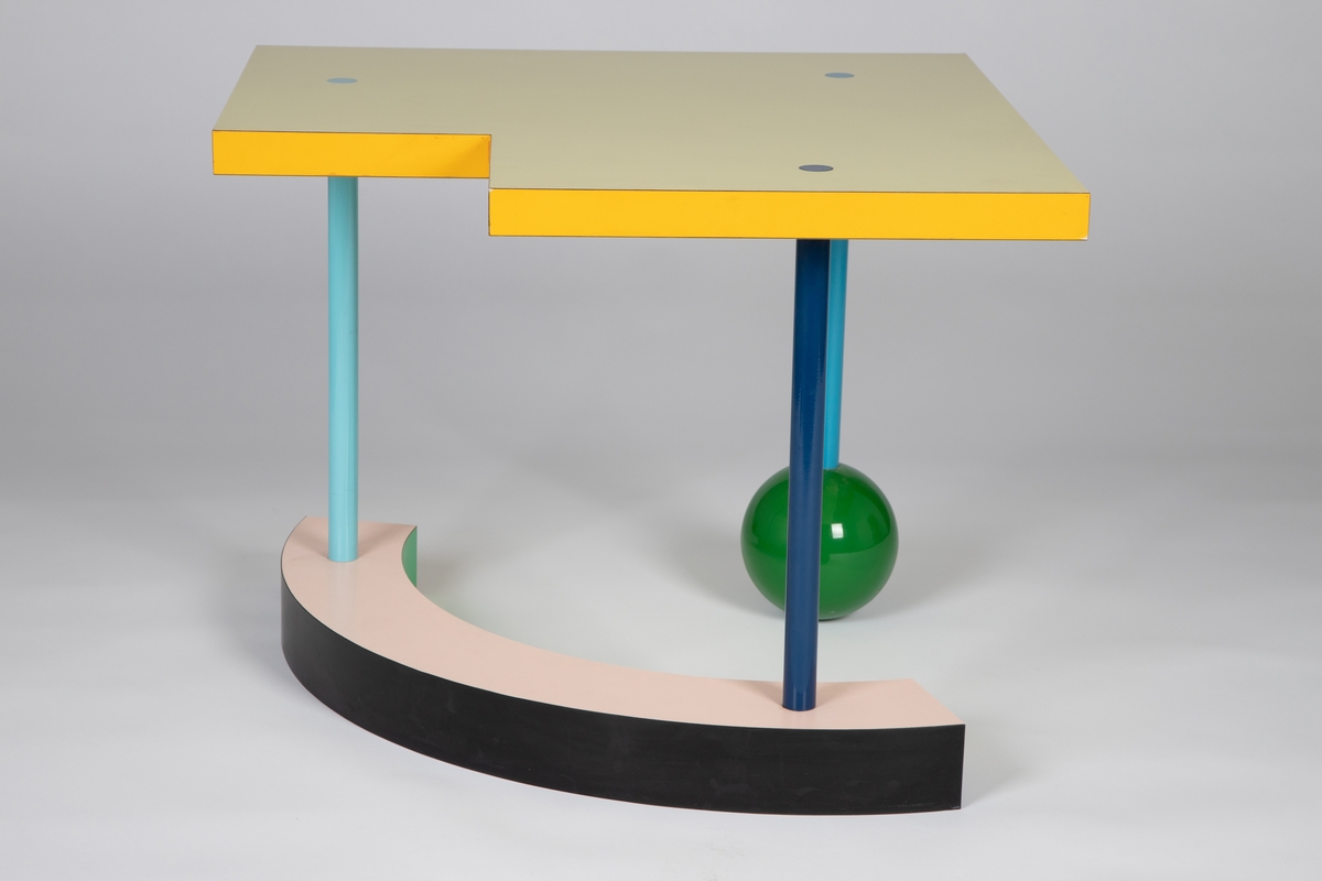 Lavt bord med sterke farger og geometriske former. Lys gul kvadratisk bordplate med et mindre kvadrat fjernet fra det ene hjørnet. De seks sidene av platetykkelsen er vekselvis røde, lilla og gule. Tre smale, rette bein i ulike blåtoner går gjennom bordplaten, med sammenføyningene som synlige sirkler i flukt med platetoppen. Det ene beinet hviler på en grønn, ganske stor kule og de to andre står på en bøyd kvartsirkelform med synlige flater i rosa, grønn, blå og svart. Med sin lekne asymmetri og mange ulike fargeflater, varierer bordets formale uttrykk stadig med synsvinkelen.