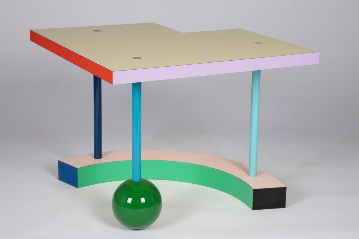 Lavt bord med sterke farger og geometriske former. Lys gul kvadratisk bordplate med et mindre kvadrat fjernet fra det ene hjørnet. De seks sidene av platetykkelsen er vekselvis røde, lilla og gule. Tre smale, rette bein i ulike blåtoner går gjennom bordplaten, med sammenføyningene som synlige sirkler i flukt med platetoppen. Det ene beinet hviler på en grønn, ganske stor kule og de to andre står på en bøyd kvartsirkelform med synlige flater i rosa, grønn, blå og svart. Med sin lekne asymmetri og mange ulike fargeflater, varierer bordets formale uttrykk stadig med synsvinkelen.