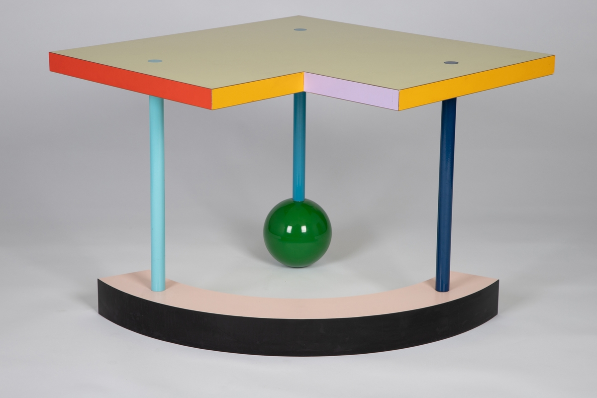 Lavt bord med sterke farger og geometriske former. Lys gul kvadratisk bordplate med et mindre kvadrat fjernet fra det ene hjørnet. De seks sidene av platetykkelsen er vekselvis røde, lilla og gule. Tre smale, rette bein i ulike blåtoner går gjennom bordplaten, med sammenføyningene som synlige sirkler i flukt med platetoppen. Det ene beinet hviler på en grønn, ganske stor kule og de to andre står på en bøyd kvartsirkelform med synlige flater i rosa, grønn, blå og svart. Med sin lekne asymmetri og mange ulike fargeflater, varierer bordets formale uttrykk stadig med synsvinkelen.