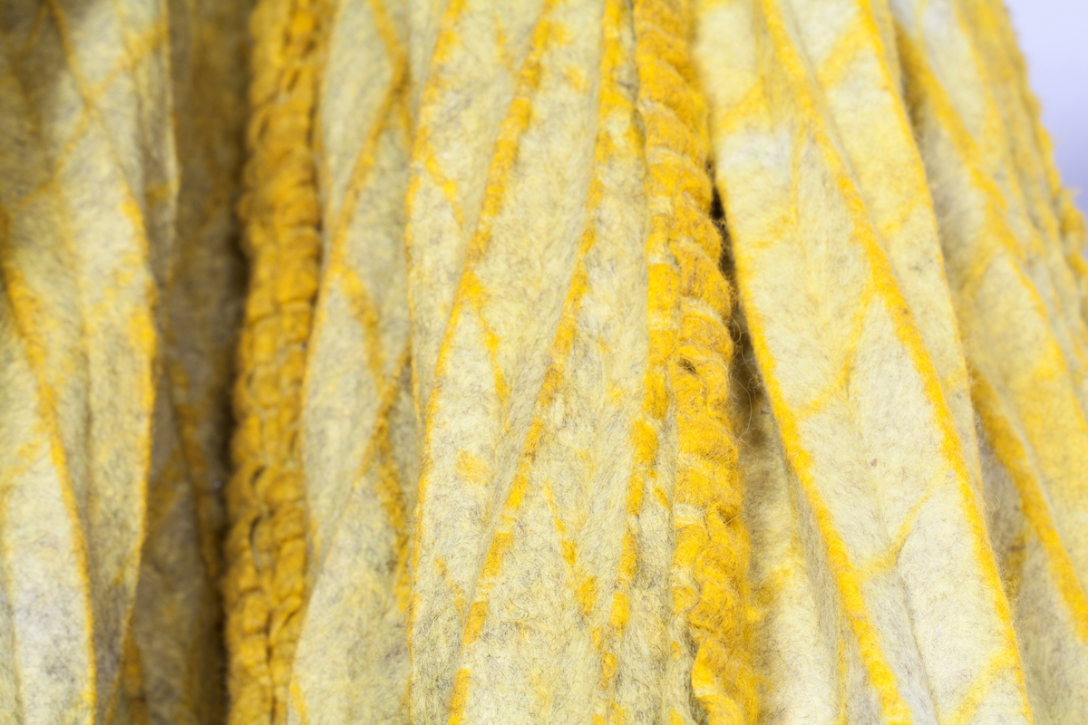 Fritthengende, tekstilt kunsthåndverk av plissert og tovet ull. Objektet er skulpturelt av uttrykk og utstyrt med løpegang øverst, og tredd på en åpen metallring. Fremstår dermed som et sylindrisk, halvveis lukket rom fra tak til gulv. Tekstilet er svært tungt og kraftig tovet, sammensatt av fire lengder. Disse er sydd sammen for hånd, slik at sømmonnene fremstår som bølgete kanter på rettsiden. Tekstilet er sennepsgult, men går nederst over i svakt limegrønt på sidene og baksiden. Det limegrønne er overskåret av parallelle og diagonale striper i skarpere grønt. Disse stripene krysser plisseringen, slik at det dannes et optisk inntrykk av rombeformede ruter.