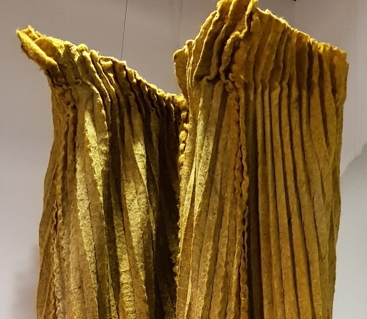 Fritthengende, tekstilt kunsthåndverk av plissert og tovet ull. Objektet er skulpturelt av uttrykk og utstyrt med løpegang øverst, og tredd på en åpen metallring. Fremstår dermed som et sylindrisk, halvveis lukket rom fra tak til gulv. Tekstilet er svært tungt og kraftig tovet, sammensatt av fire lengder. Disse er sydd sammen for hånd, slik at sømmonnene fremstår som bølgete kanter på rettsiden. Tekstilet er sennepsgult, men går nederst over i svakt limegrønt på sidene og baksiden. Det limegrønne er overskåret av parallelle og diagonale striper i skarpere grønt. Disse stripene krysser plisseringen, slik at det dannes et optisk inntrykk av rombeformede ruter.