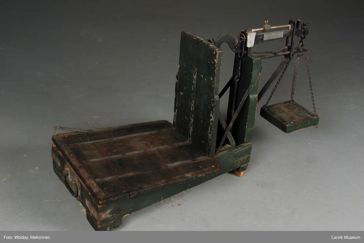 Vektstativ av tre med forsterkninger av jern. Løfte/bære håndtak på den ene siden. 2 - 200 kg.
Vektskål med 4 kjettinger henger i en krok.
4 lodd.