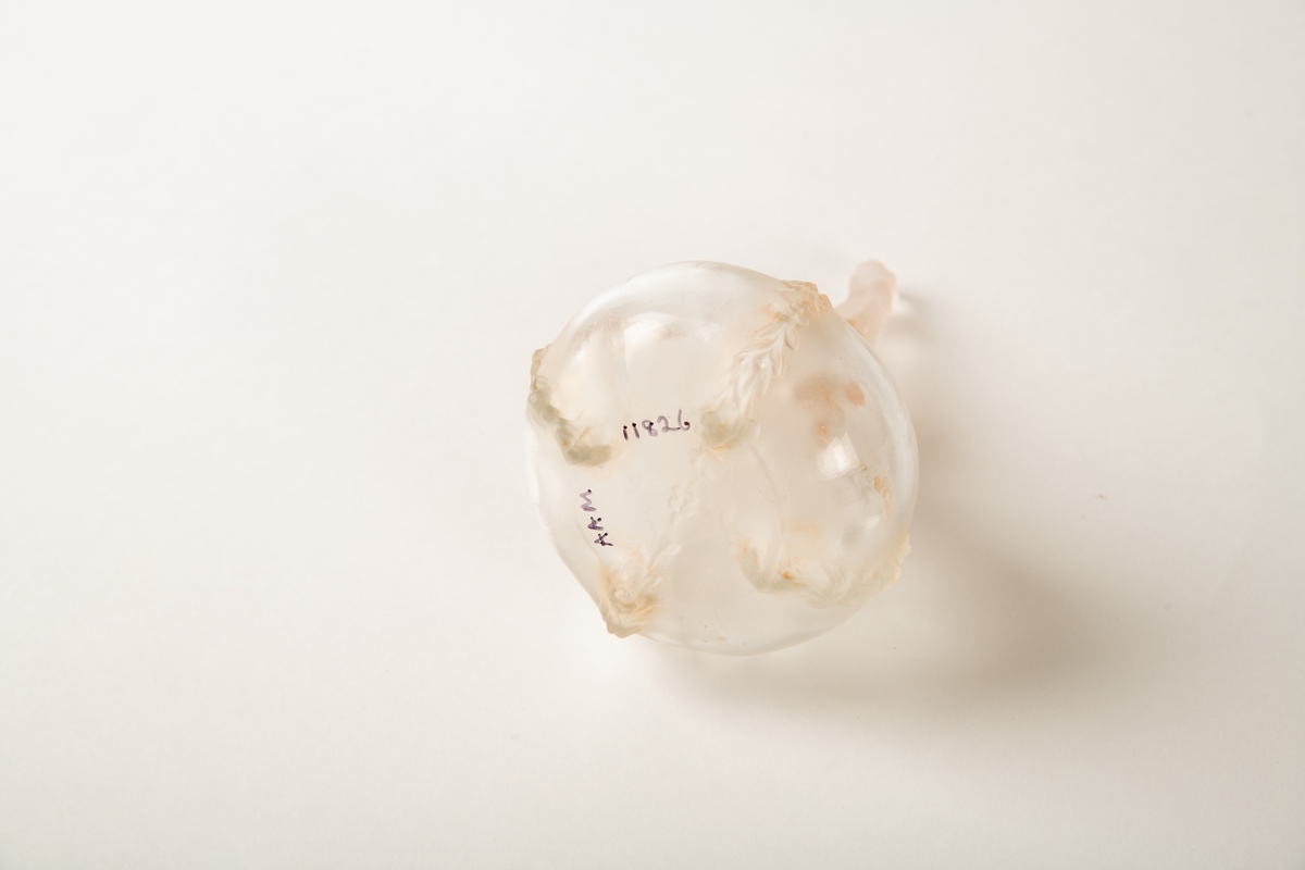 Rund krukke med fire blomsterranker i relieff ned siden. Liten munning med propp, hvorpå en  sittende kvinne på en slange. Inngravert:  Eva.