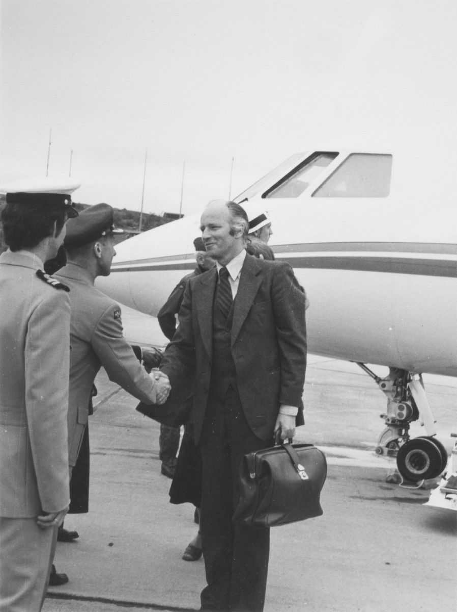 Lufthavn (flyplass). Detaljfoto av et fly med landgang. Forvarsminster Thorvald Stoltenberg hilser på en person i uniform.