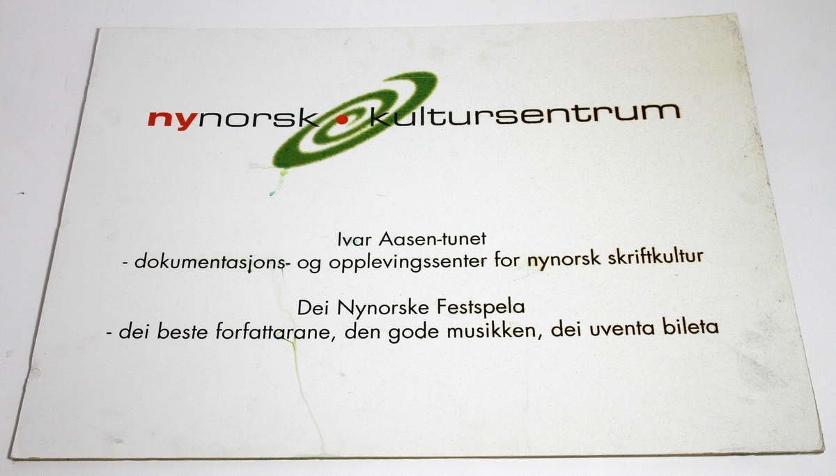 Papplate med logoen til Nynorsk kultursentrum på. Denne logoen vart truleg danna i 2000 eller 2001. På plata står det informasjon om Nynorsk kultursentrum, Ivar Aasen-tunet og Dei nynorske festspela.