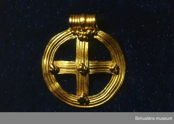 Ett hängsmycke, i orm av ett ringkors av guld med fast ögla. Korset är likarmat och placerat i en ring av samma bredd som korsarmarna. På framsidan är ytan dekorerad med längsgående, något oregelbunden räffling. Korsmitten och korsarmarnas anslutningspunkter dekorerade med granulering (små kulor). 
Smycket dateras till folkvandringstid, 400 - 600 e. Kr. och brukar kallas för "Rörakorset". 

Landskap BOHUSLÄN
LÖSFYND