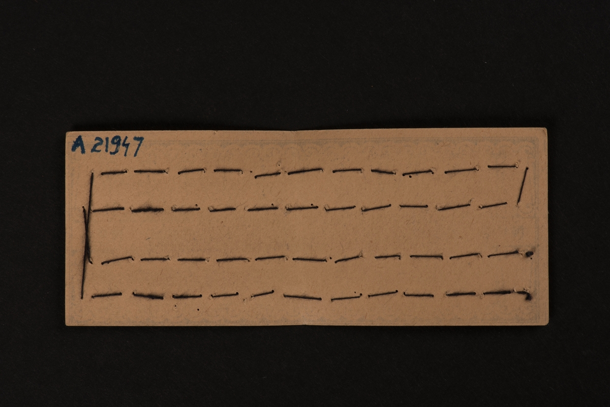 En karta av papp med fastsydda hyskor och hakar av metall. Två rader, med tjugofyra hakar och hyskor. Kartan är dekorerad med ett tryckt mönster, samt "GUSUM No 2". I mitten en svan över texten "FABRIKS-MÄRKE" inom en romb.