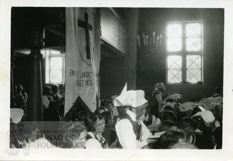 Folk i bunad i en kirke. Flere kvinner i hardangerskaut.