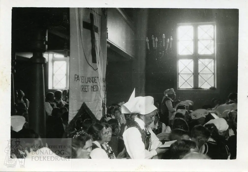 Folk i bunad i en kirke. Flere kvinner i hardangerskaut.