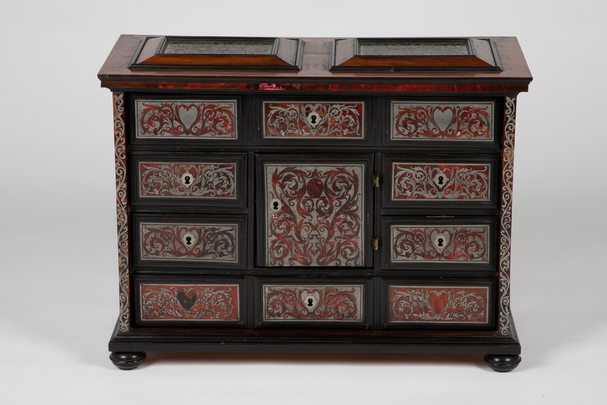 Kabinett med kuleben og profilert fotlist. Fronten har 10 skuffer omkring en dør i midten, innrammet av profilerte lister av ibenholt. Alle fyllinger har marketeri i "Boulle-teknikk", bestående av skilpadde og tinn. som er gravert med akantusranker. Sidelister, topplatens to fyllinger og sidenes to fyllinger har alle marketeri i tilsvarende teknikk med ranker. Profilert topplist med kant av skilpadde. Tre skuffer bak midtdøren.