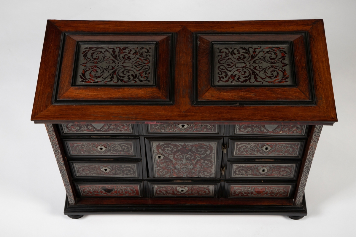 Kabinett med kuleben og profilert fotlist. Fronten har 10 skuffer omkring en dør i midten, innrammet av profilerte lister av ibenholt. Alle fyllinger har marketeri i "Boulle-teknikk", bestående av skilpadde og tinn. som er gravert med akantusranker. Sidelister, topplatens to fyllinger og sidenes to fyllinger har alle marketeri i tilsvarende teknikk med ranker. Profilert topplist med kant av skilpadde. Tre skuffer bak midtdøren.
