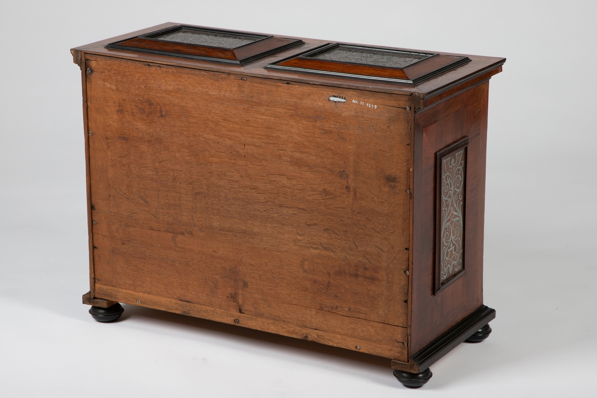 Kabinett med kuleben og profilert fotlist. Fronten har 10 skuffer omkring en dør i midten, innrammet av profilerte lister av ibenholt. Alle fyllinger har marketeri i "Boulle-teknikk", bestående av skilpadde og tinn. som er gravert med akantusranker. Sidelister, topplatens to fyllinger og sidenes to fyllinger har alle marketeri i tilsvarende teknikk med ranker. Profilert topplist med kant av skilpadde. Tre skuffer bak midtdøren.