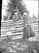 Kvinna står med Ruth Skötsner vid gärdesgården och ett barn sitter på marken, Östhammar Uppland