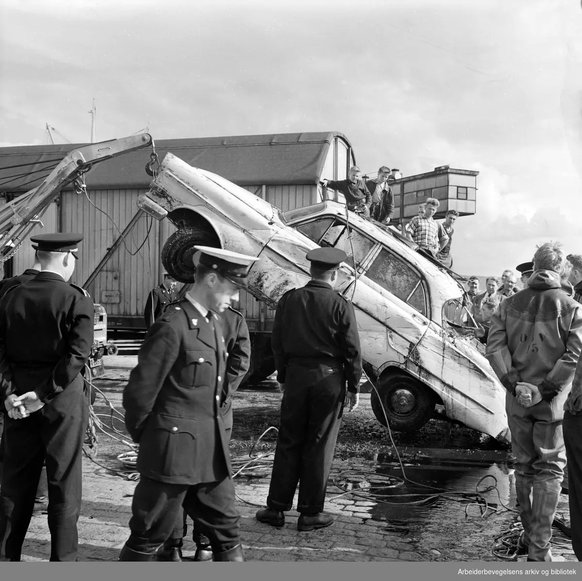 Dykkere fra Oslo Brannvesen heiser i land et bilvrak ved kaia på Vippetangen. August 1962.