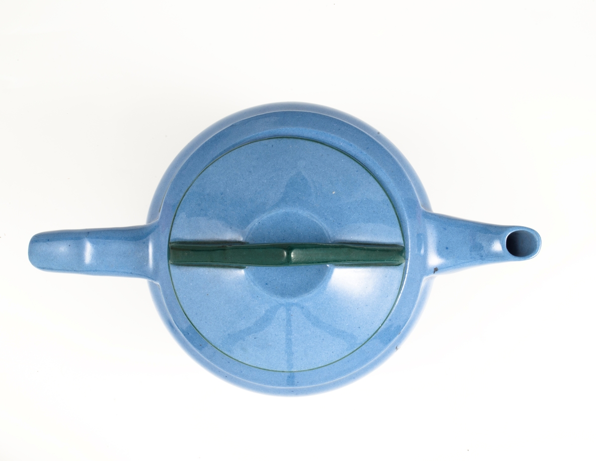 Tekanne med lokk i glasert steingods med begitning. Tilnærmet kuleformet lyseblått korpus med påsatt vinkelformet hank, samt en smal trekantformet tut med sirkulær åpning. Nedre del av korpus er dekorert med en stilisert bord i grønt og rødt. Horisontale grønne linjer understreker kannens form. Den avsluttes med et sirkulært lokk som krones med en triangulær grønnfarget lokknapp.