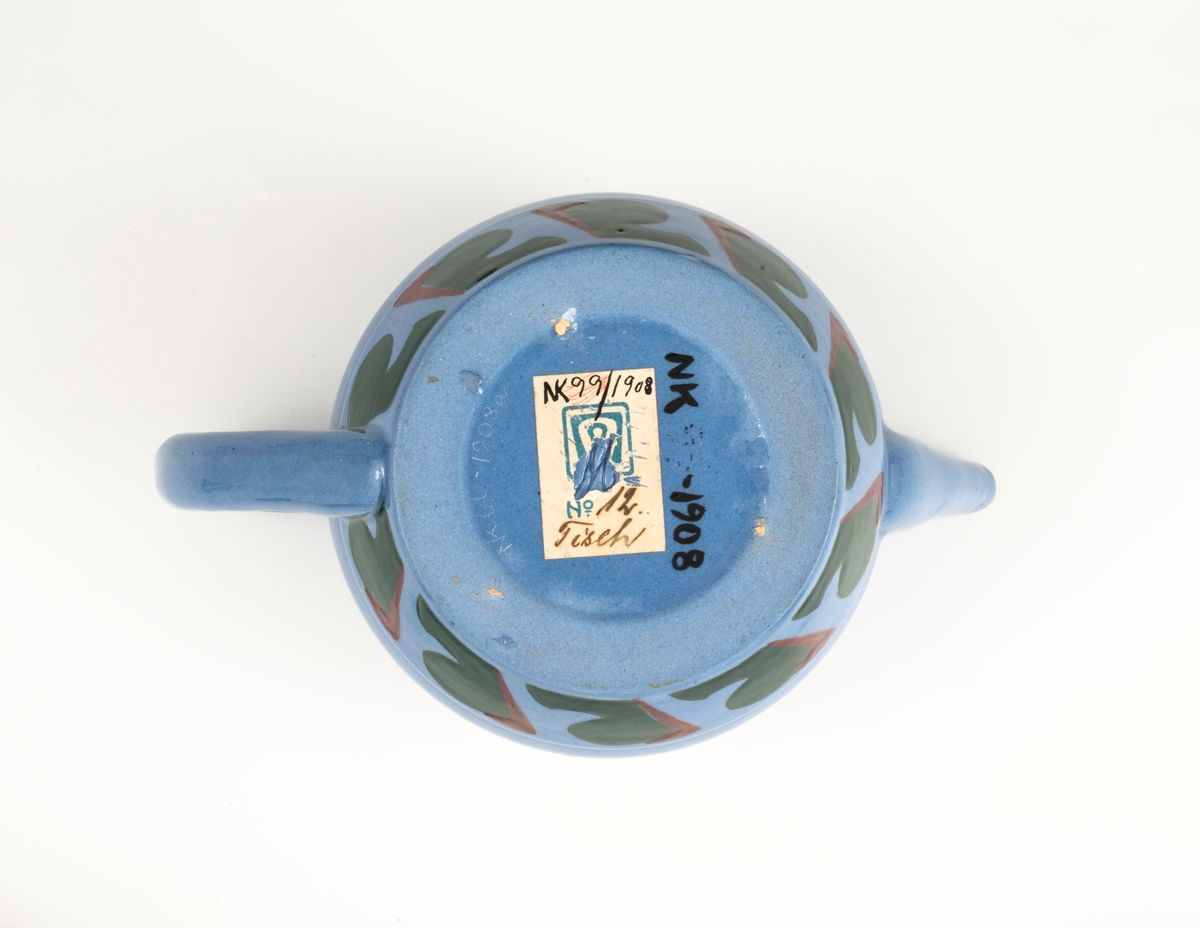 Tekanne med lokk i glasert steingods med begitning. Tilnærmet kuleformet lyseblått korpus med påsatt vinkelformet hank, samt en smal trekantformet tut med sirkulær åpning. Nedre del av korpus er dekorert med en stilisert bord i grønt og rødt. Horisontale grønne linjer understreker kannens form. Den avsluttes med et sirkulært lokk som krones med en triangulær grønnfarget lokknapp.