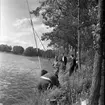 Män står utmed med en strand med metspön.