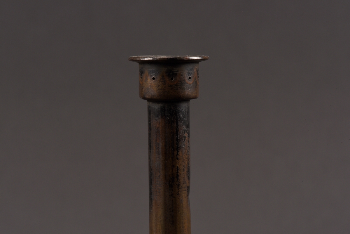 Cylindrisk gasoljelampa tillverkad av mässing. I mitten en cylindrisk vekhållare som är fäst i gängat påfyllnadslock. På sidorna av oljehuset sitter två cylindriska upphöjningar med oklar funktion. Den ena är öppningsbar och locket har ursprungligen varit förankrad i oljehuset via en länk.