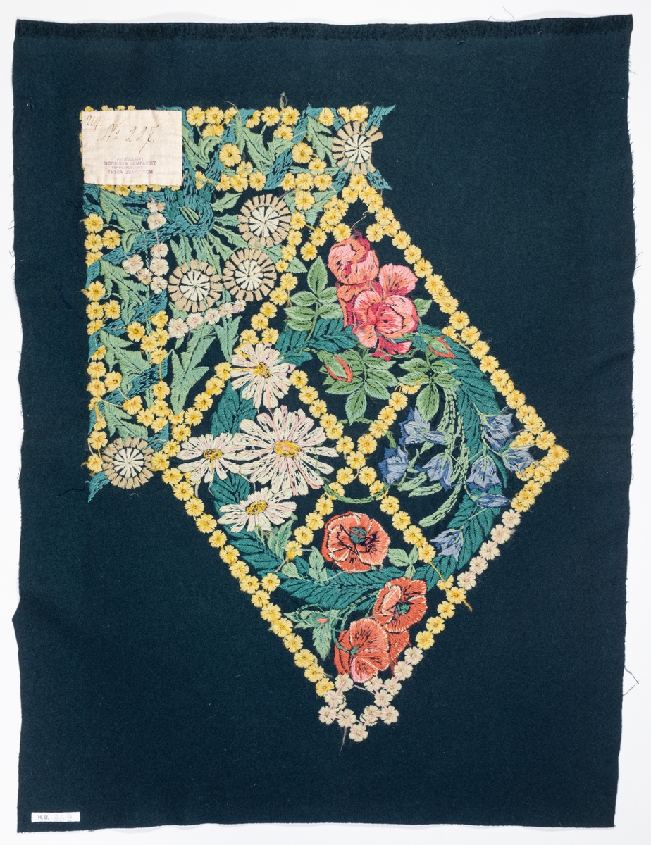 Påbörjad dyna, 80 x 58. Broderi i schattersöm i ullgarn i ljusa färger på blått kläde. Parti ur stor bonad av Ferdinand Boberg. Blommor och bladverk i fält inramat av gullvivor. Ljusgult, vitt, grönt, blått, rött m.fl. färger.